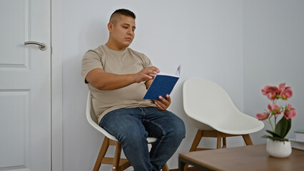 Handsome latin man, immersed in a book, comfortably sitting in a lobby chair. a young, relaxed...