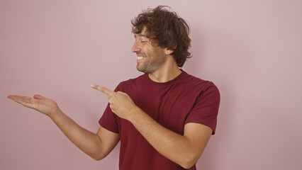 A smiling hispanic man with a beard presents with his hand against a pink background, conveying a friendly demeanor.
