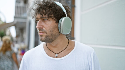 A pensive hispanic man with headphones outdoors in an urban setting, evoking a sense of modern...