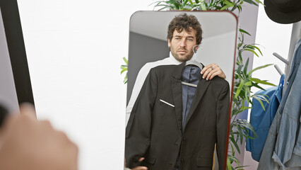 A handsome young man with a beard trying on a suit in a dressing room, reflected in a mirror