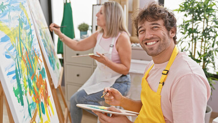 Two confident artists, man and woman, enjoy drawing together with smiles in indoor art studio,...