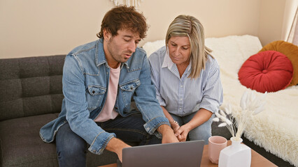 Mother and son sharing a heart-warming tech moment on their home sofa, speaking and using a laptop together in their casual sitting