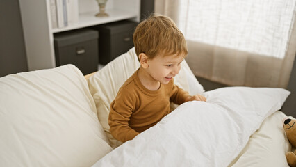 A smiling young boy plays on a bed in a well-lit cozy bedroom, embodying innocence and joy.