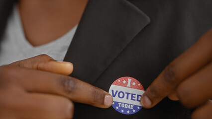 African american woman attaching an 'i voted today' sticker to her blazer in an indoor setting