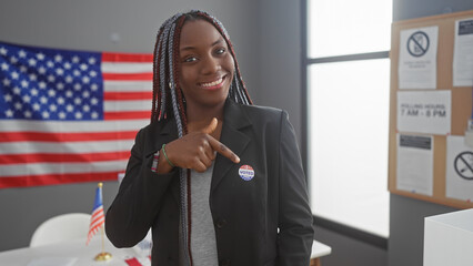 A smiling african american woman with braids points to her 'i voted' sticker in a room with an...