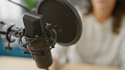 Focused woman records podcast using professional microphone in a modern studio.