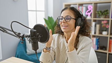 Smiling hispanic woman recording with microphone in radio studio interior.