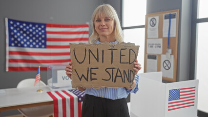 Blonde woman holding sign 'united we stand' in american voting center with us flag.