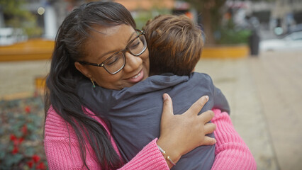 A smiling woman hugs a boy outdoors, showcasing a loving moment between mother and son in an urban park.