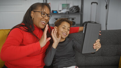 A woman and a boy sharing a joyful moment with a tablet in a cozy living room, epitomizing family...