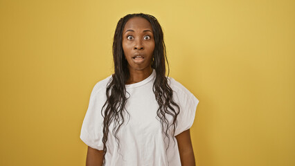 Surprised young african american woman with long curly hair wearing a white t-shirt against a...