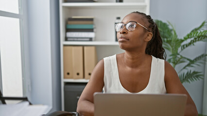 Contemplative young woman with glasses in a modern office interior, looking away thoughtfully.