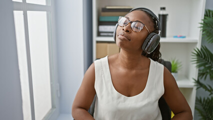 Relaxed african american woman enjoying music with headphones in a modern office interior.