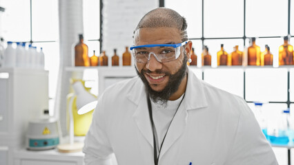 Handsome african american male scientist with beard wearing lab coat and protective glasses in...