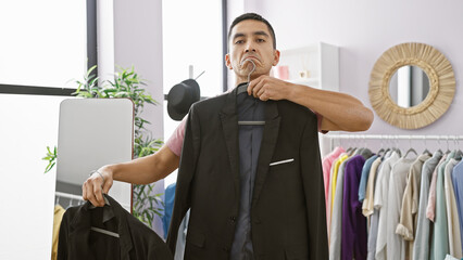 Handsome hispanic man trying on suit in a modern wardrobe room with mirror and clothing rack.