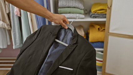 A hand holds a hanger with a elegant suit in a tidy wardrobe full of clothes.