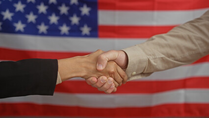 Man and woman shaking hands in an office with an american flag backdrop, symbolizing cooperation.