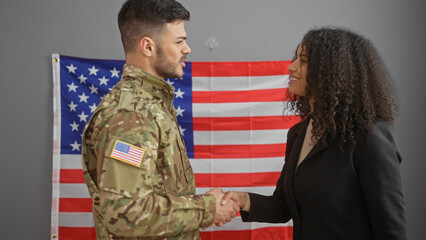 A man in military uniform shaking hands with a woman in an office, with the us flag in the...