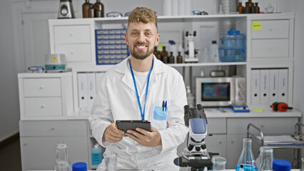Caucasian scientist with beard and blue eyes in lab coat uses tablet in laboratory