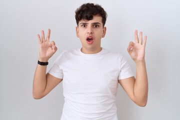 Young non binary man wearing casual white t shirt looking surprised and shocked doing ok approval...