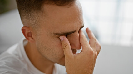 Fototapeta premium A thoughtful young hispanic man indoors touching his face, showcasing stress, contemplation, or health concerns.