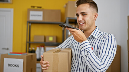 A young hispanic man holds a package in a warehouse interior, speaking on a smartphone.