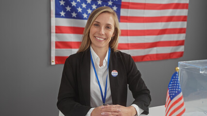 Smiling woman with a 'voted' sticker, american flag backdrop in a voting center.