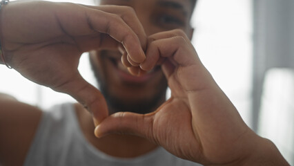 A smiling african american man making a heart shape with his hands indoors.