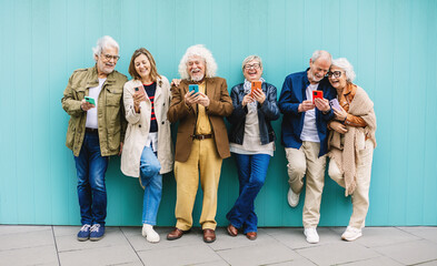 Happy senior adult people using mobile phones standing over isolated blue background. Communication and elderly lifestyle concept.