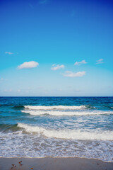 waves crashing on beach with clouds in blue sky