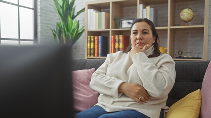 Mature hispanic woman contemplating in a cozy living room, evoking a serene ambiance.
