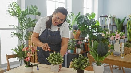 Smiling woman arranges plants in a bright flower shop while talking on the phone