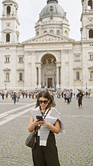 A stylish latina woman uses a smartphone in front of budapest's st. stephen's basilica