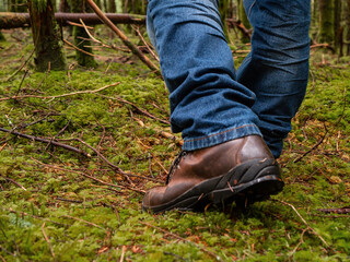 Tourist in blue jeans and tough brown leather outdoor boots on a green moss in a dense forest. Trip...