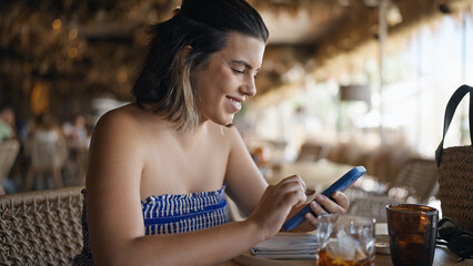 Young hispanic woman smiling happy using smartphone sitting on the table at the restaurant