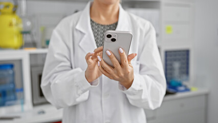 Hands of determined woman scientist tapping on smartphone amidst the hum and fervor of technology-ridden laboratory work