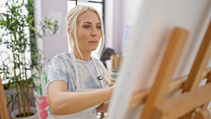 Passionate young blonde woman artist captivatingly drawing her masterpiece at art studio