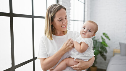 Confident mother standing in a living room, lovingly holding her smiling baby daughter in her arms, sharing a happy moment at home together