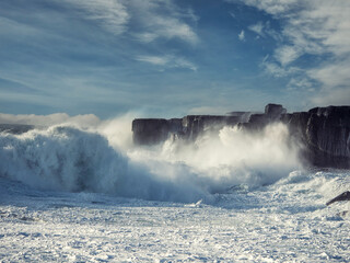 Powerful tall ocean wave hit stone cliff and create huge splash of water. County Clare, Ireland. Storm weather. Rough sea. Power of nature. Irish landscape scene. Cloudy sky.