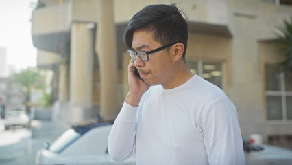 A young asian man calling on a cellphone outdoors on a city street.