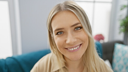 Fototapeta premium Confident young blonde enjoying relaxation, smiling while sitting comfortably on cozy sofa at home