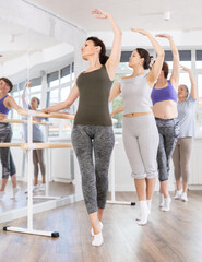 Positive woman in casual sportswear practicing graceful ballet moves during amateur group class in spacious light-filled studio