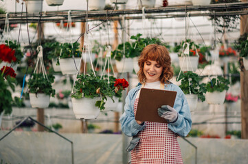 Florist in uniform at hothouse writing on clipboard and making order.