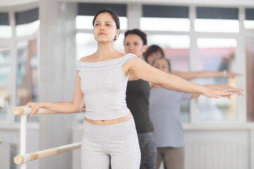 Group of female beginners practicing second ballet position at barre in dance studio