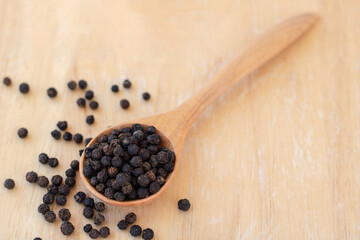 Whole black pepper on wooden spoon