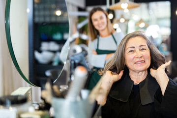 Aged woman approving result of hairdresser work, looking satisfied with new hairdo