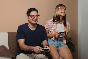 Latin adult couple playing video games on the couch in the living room, couple pastime concept on...
