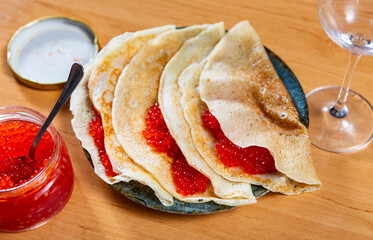 Thin crepes served in a plate with red caviar and other table appointments