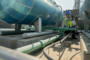 Naklejka premium Engineer in safety gear conducts inspection on large industrial water tanks on a building rooftop. Professional engineer meticulously checks connectivity and status of piping on an urban rooftop.
