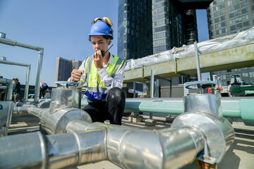 engineer inspecting HVAC equipment with a tablet on a building rooftop. An engineer attentively...